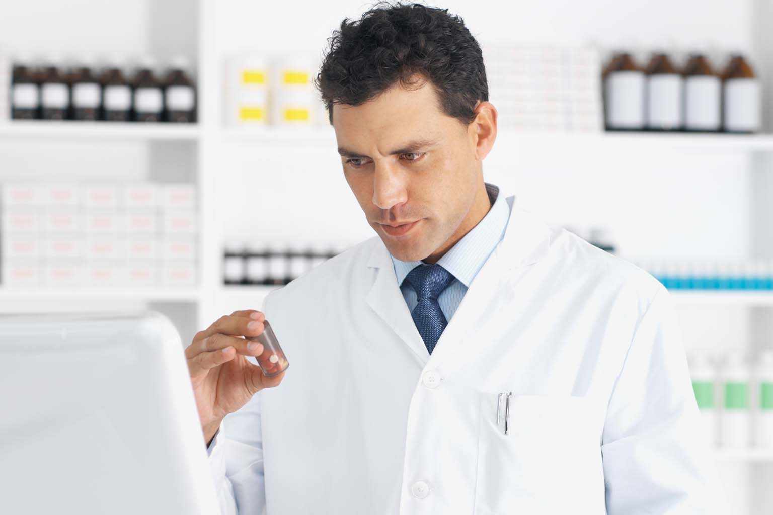 phamacist holding bottle of pills while using computer