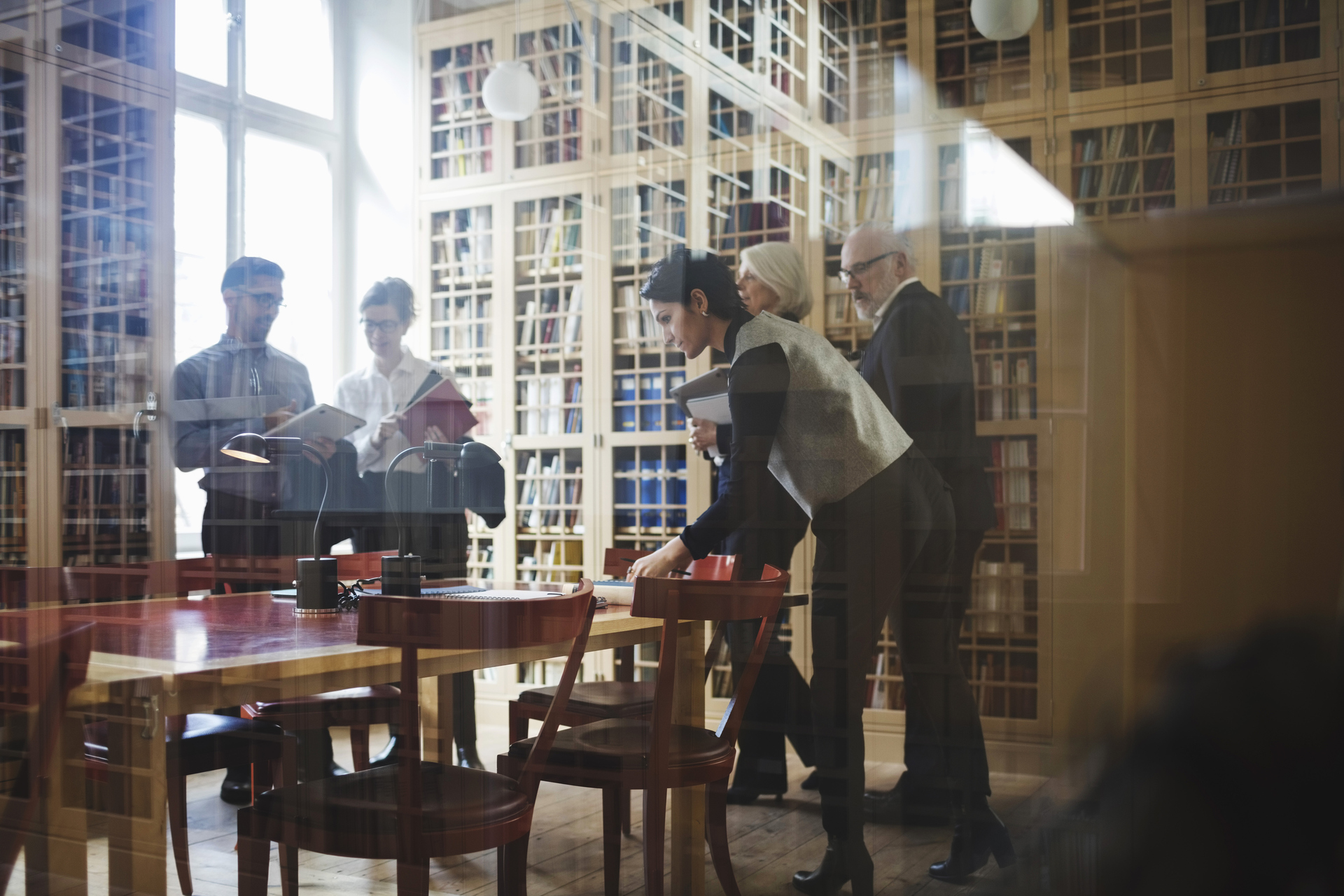 Five people in formalwear including active seniors to discuss a case near the bookshelf at law firm in Europe