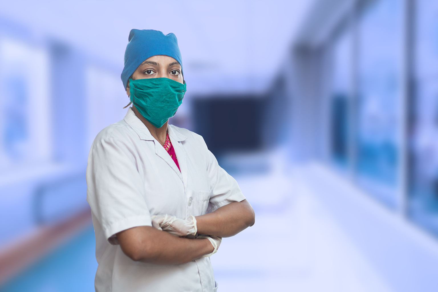 Portrait of female medical worker doctor wearing surgical mask and cap standing crossed arms outside hospital corridor covid-19 coronavirus pandemic