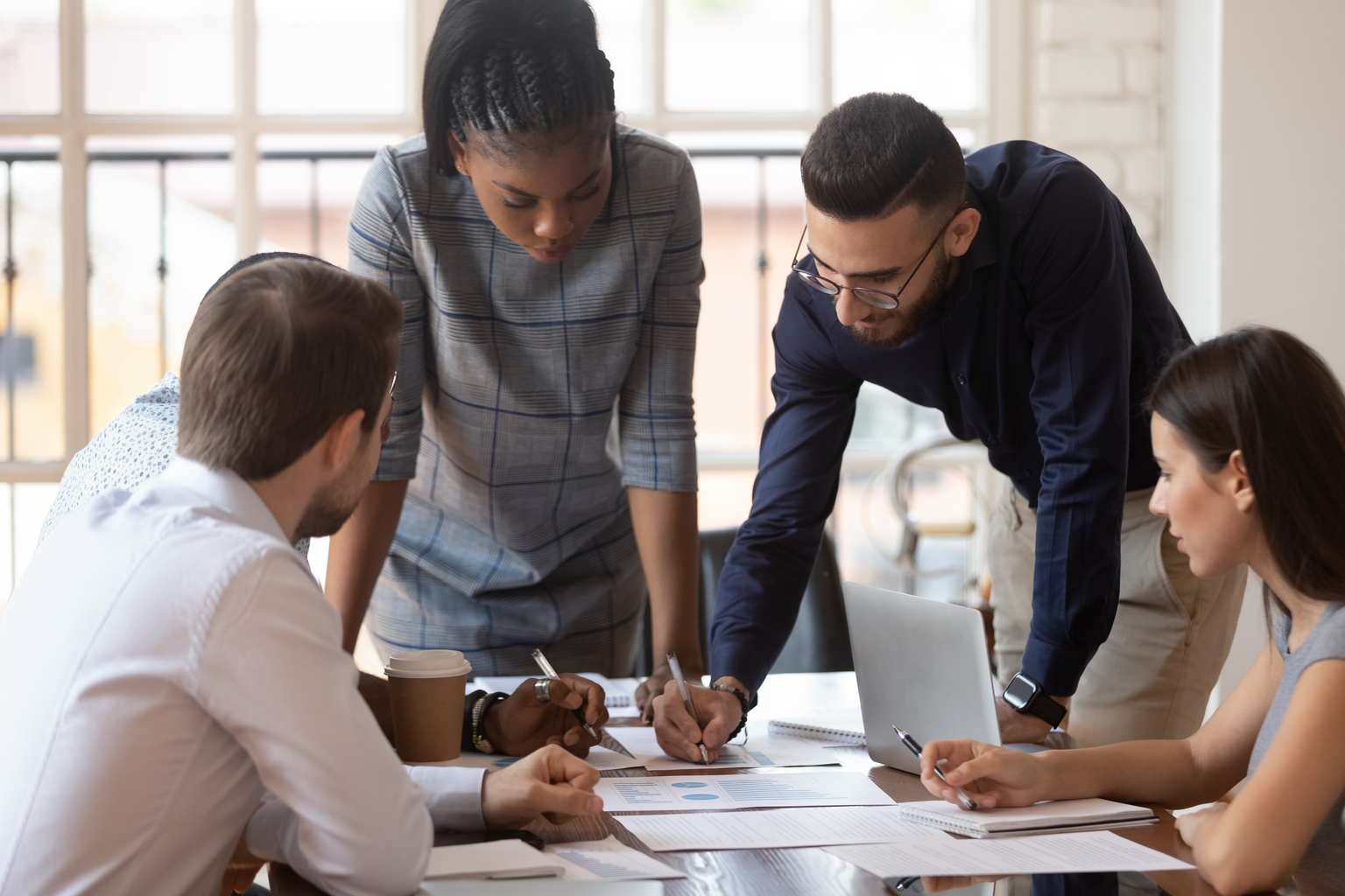 Focused multiracial corporate business team people brainstorm on marketing plan financial report gather at office table meeting, diverse serious colleagues group discuss paperwork engaged in teamwork