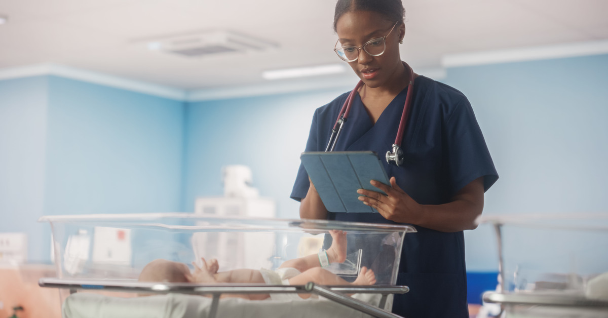 Young African nurse using tablet computer checking up on a newborn baby in maternity ward facility