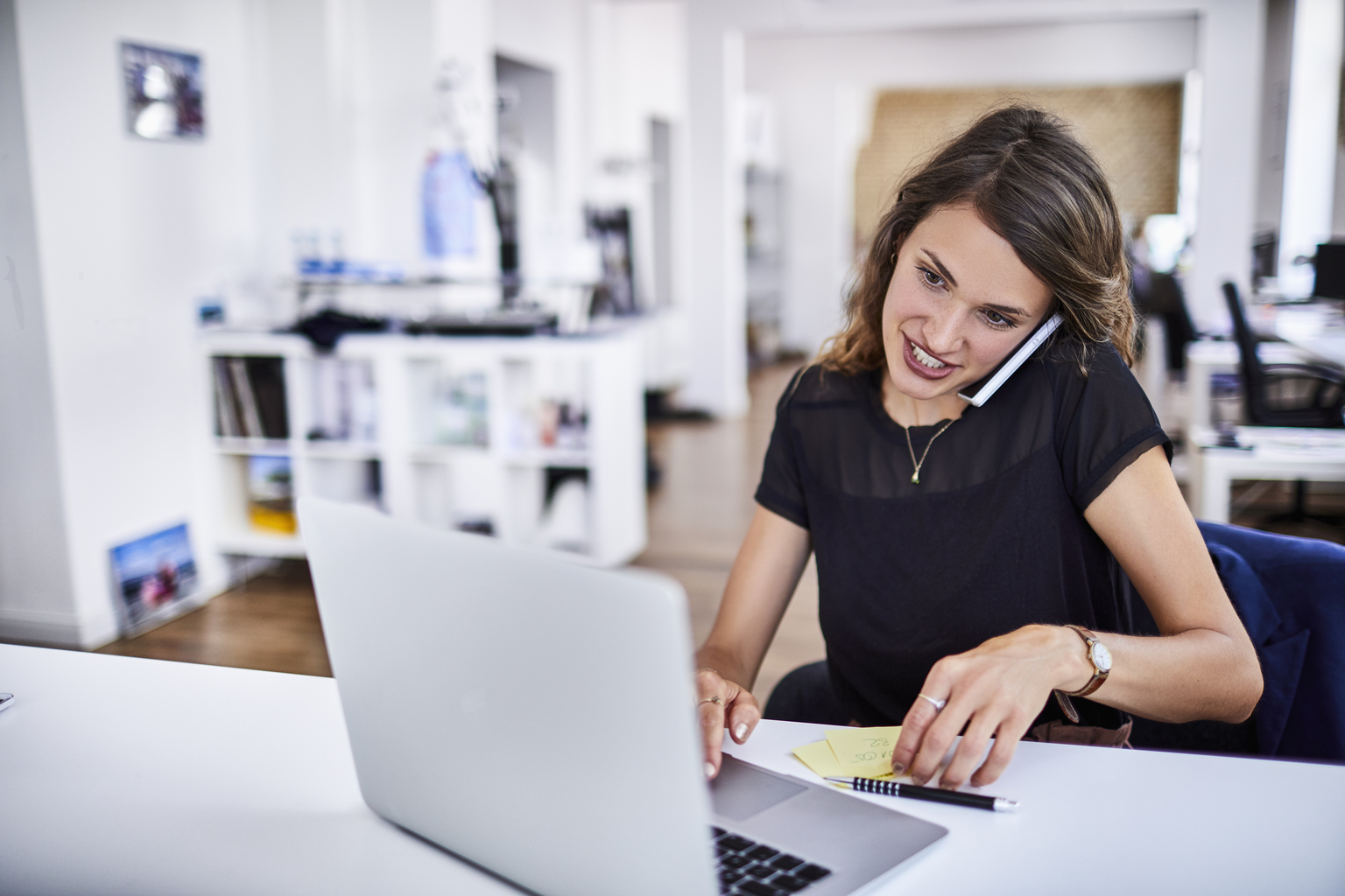 A woman talking on the phone using laptop and post-it notes from home