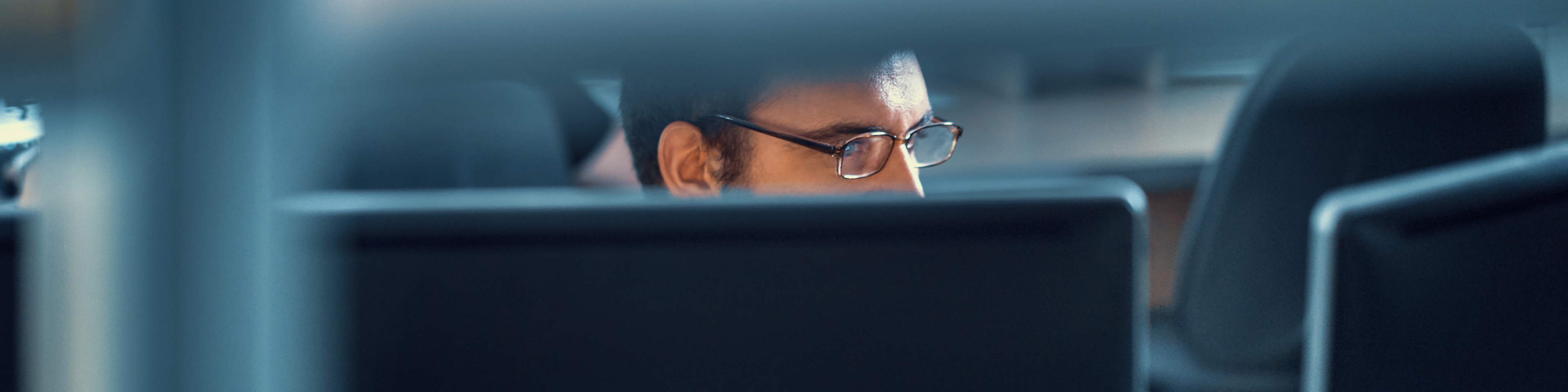 Closeup front view of deeply focus developer working on an application. He's sitting in front of dual display monitor, barely visible through office furniture