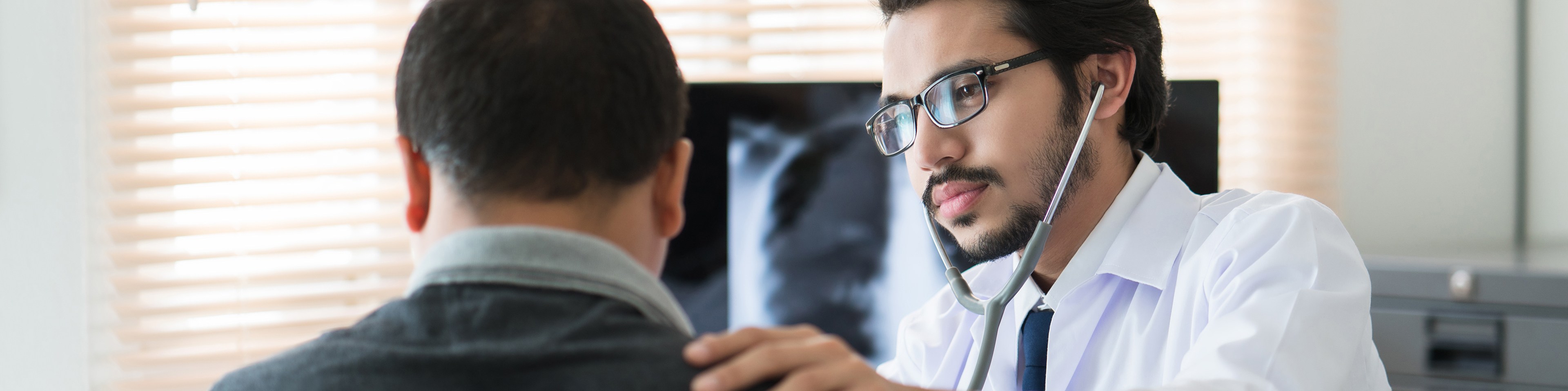 Doctor sitting with patient, checking patient with stethoscope