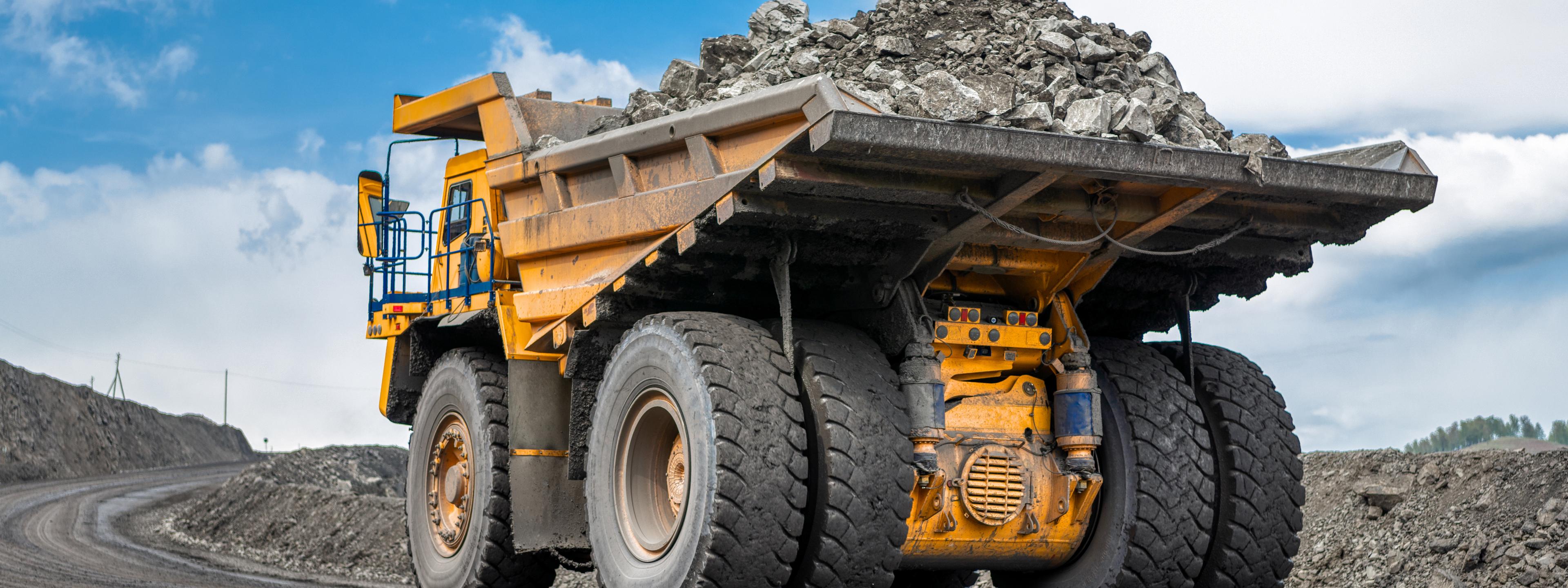 Rock transportation by dump trucks. Large quarry yellow truck. Transport industry. Mining truck is driving along a mountain road.