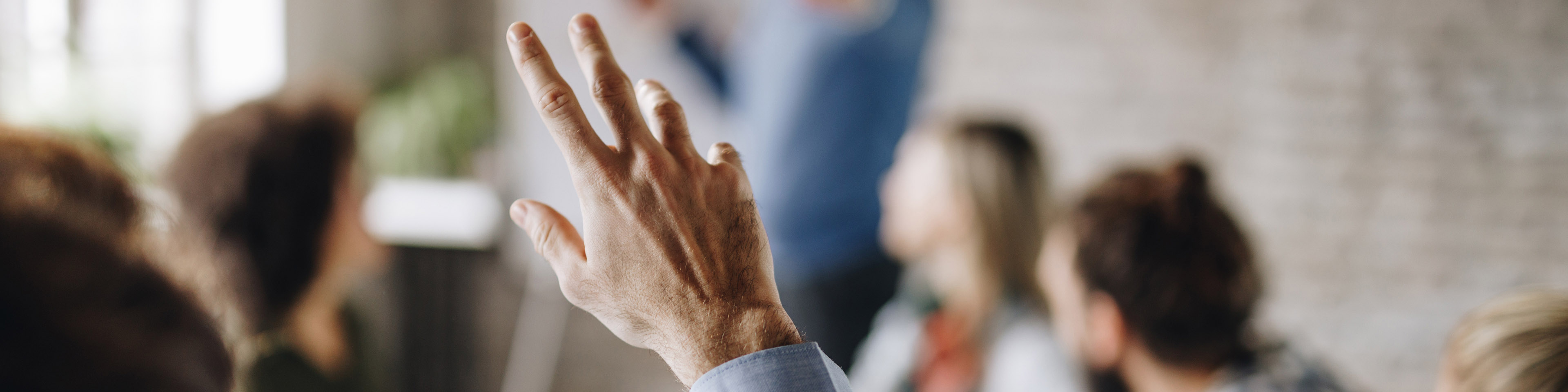 Unrecognizable person raising his hand to ask a question on a business meeting in the office.