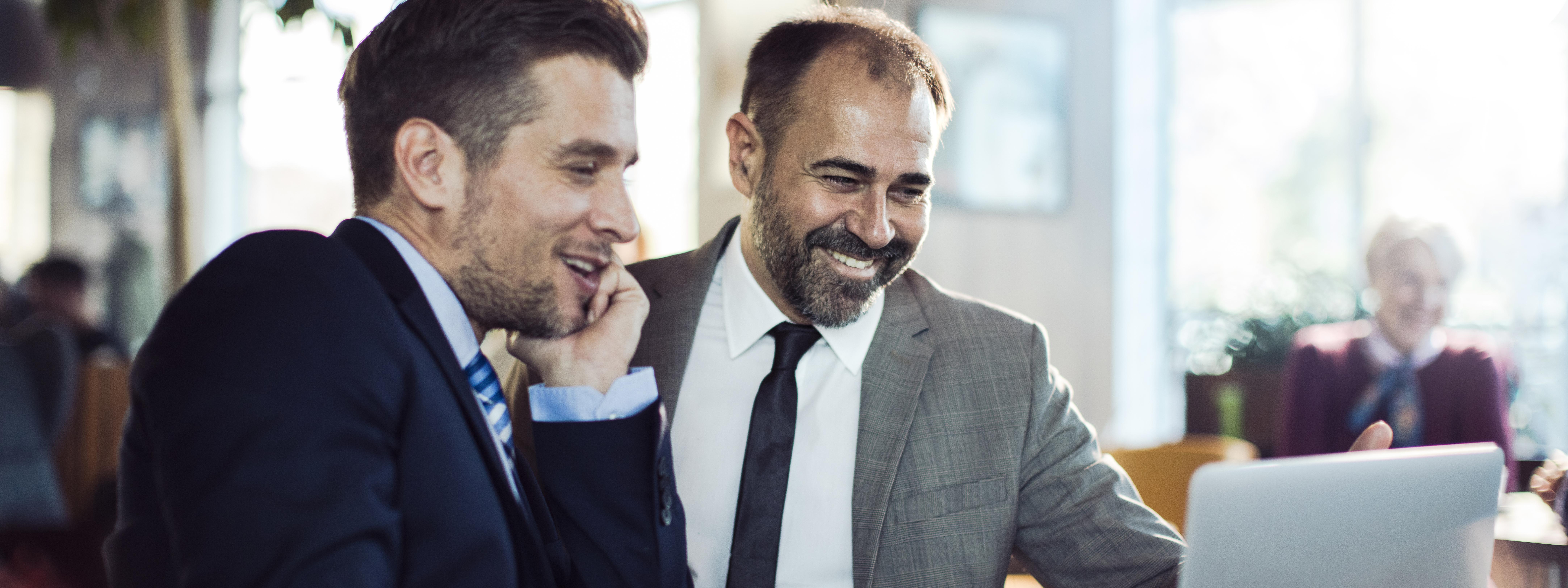 Colleagues smiling with a cup of coffee and discussing over a Laptop