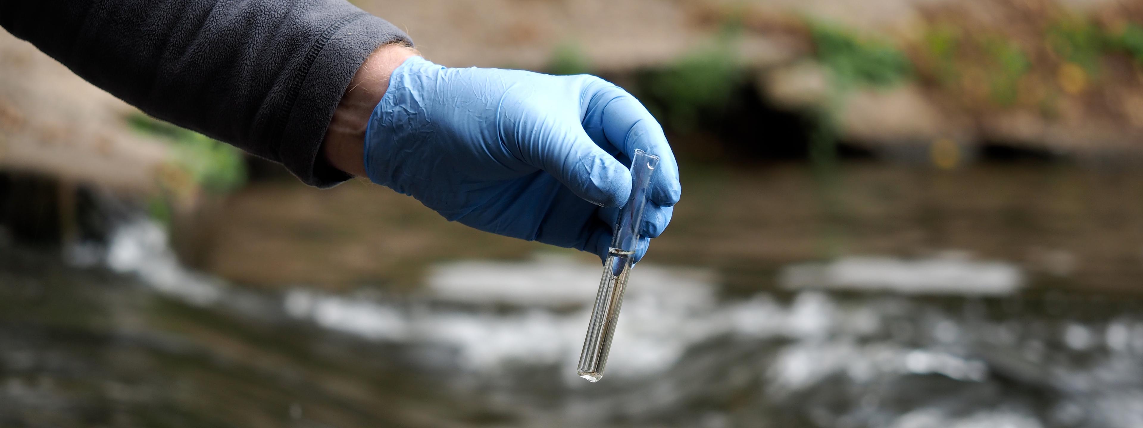 Water sample. Gloved hand into the water collecting tube. Analysis of water purity, environment, ecology - concept. Water testing for infections, harmful emissions