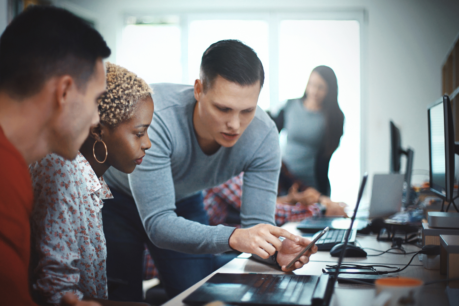 Multi-ethnic people looking at device and working together at office