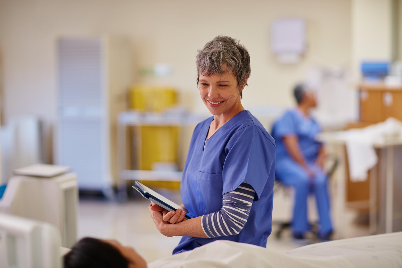 Friendly nurse stands at patient bedside holding tablet