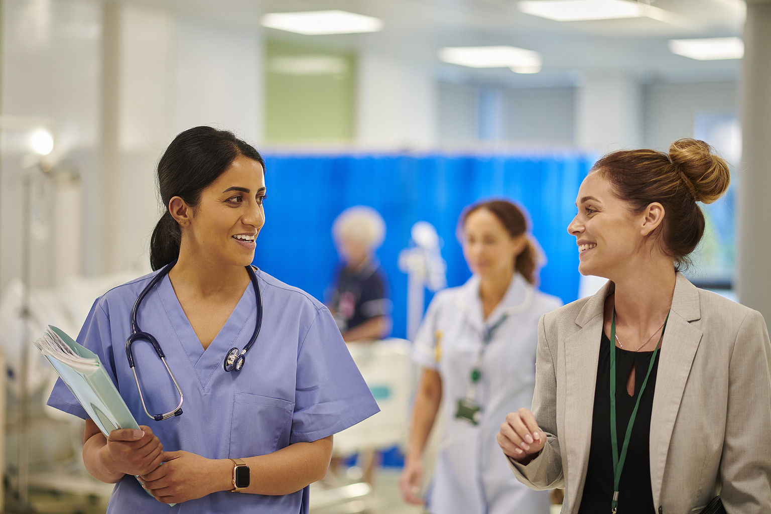 A nurse wearing scrubs talking to hospital administrator as they walk through hospital floor