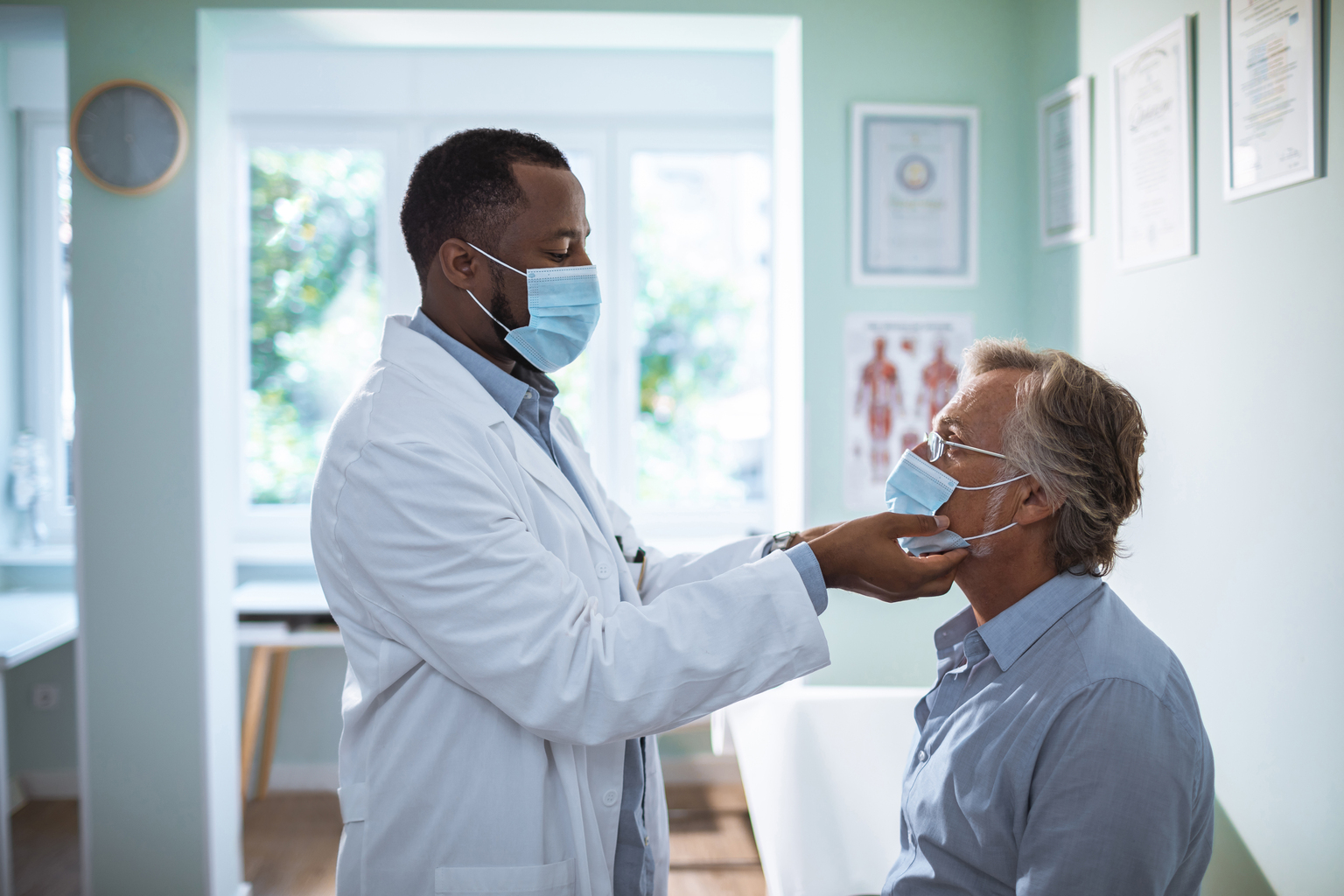 African male doctor examining a mature white male patient, both in masks.