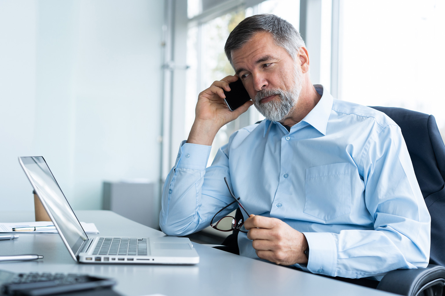 Manager w szpitalu rozmawia przez telefon i patrzy na laptop z otwartym programem Progmedica