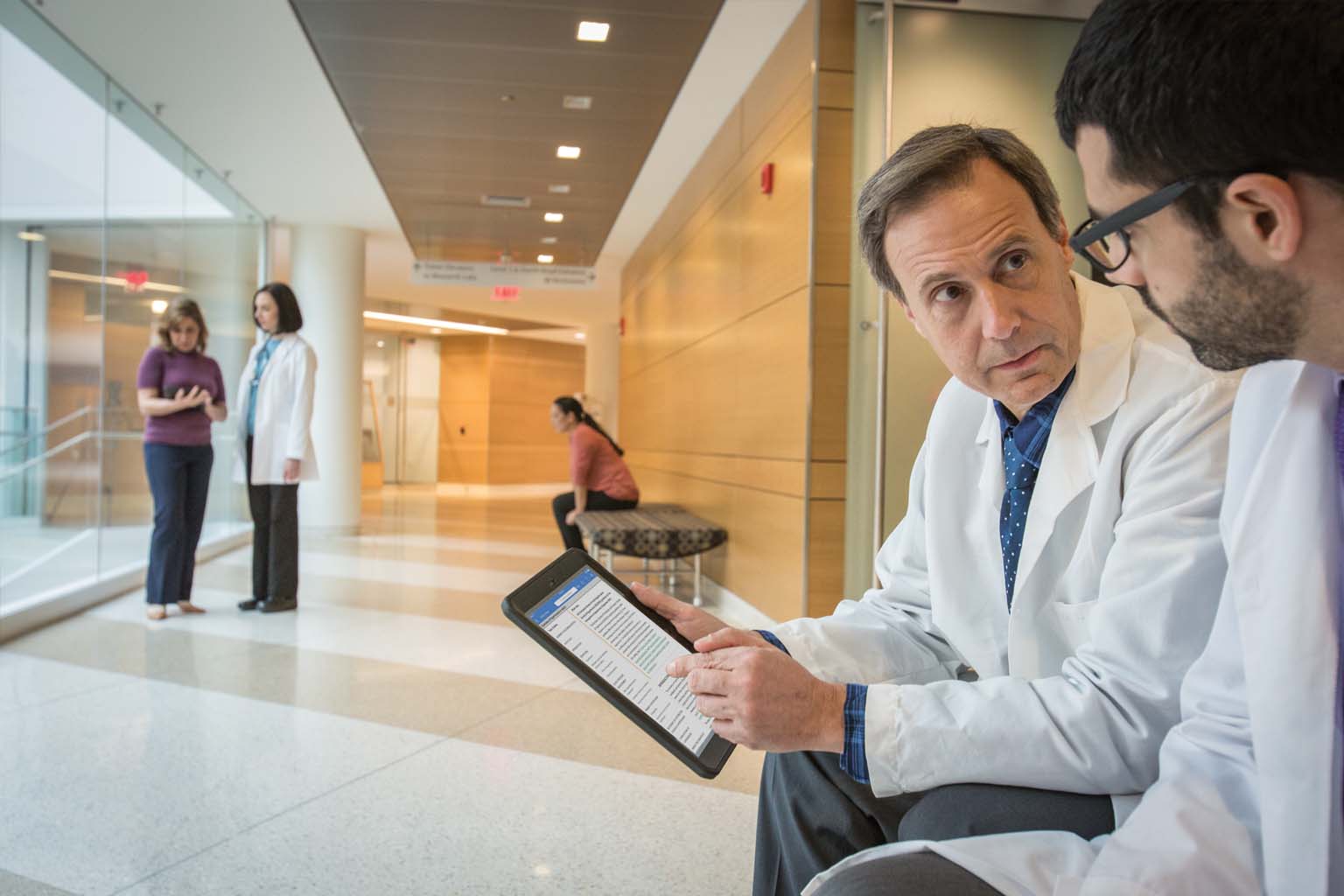 two doctors seated with tablet in hospital hallway