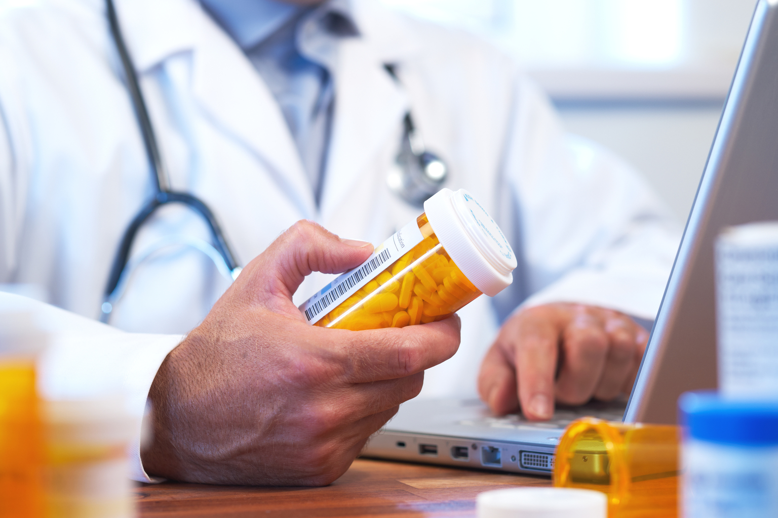 phamacist holding bottle of pills while using computer