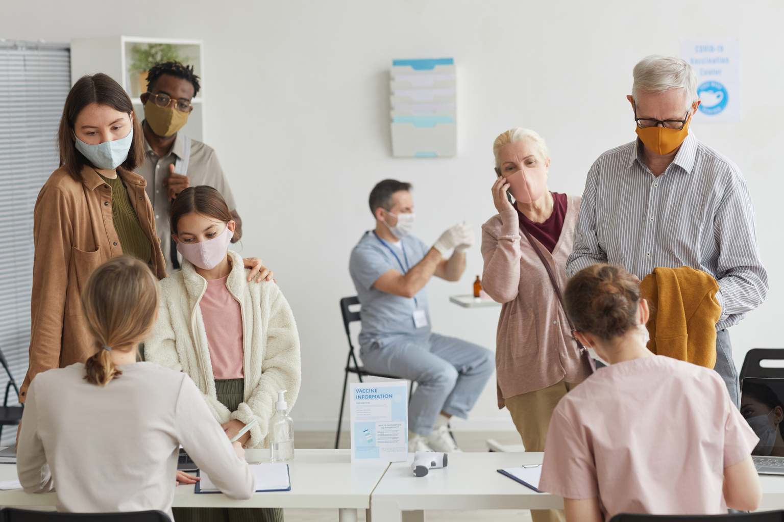 Group of patient wearing face masks, standing in lines at vaccine check in desk