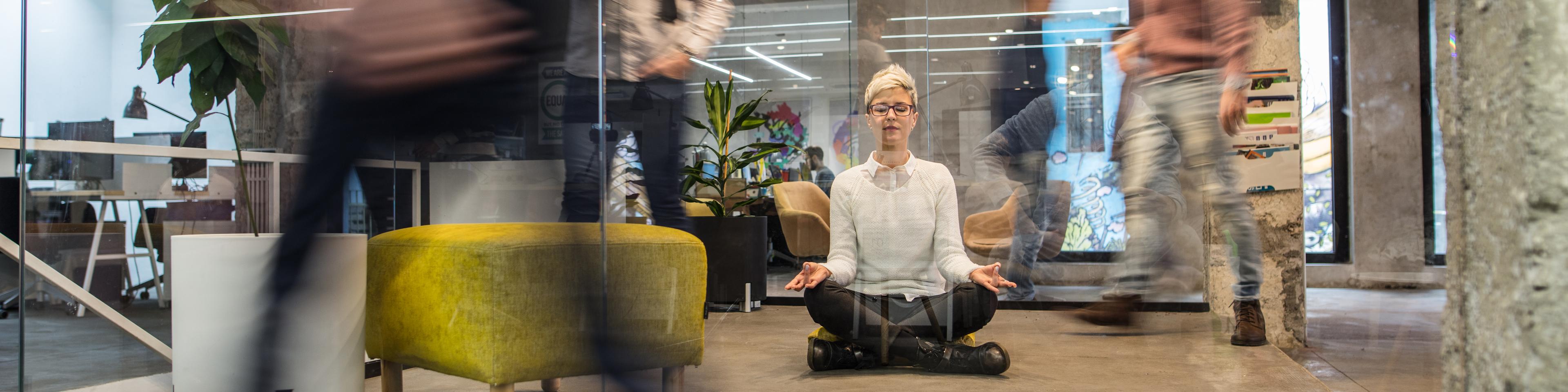 Jonge vrouwelijke ondernemer mediteert met gesloten ogen in druk kantoor