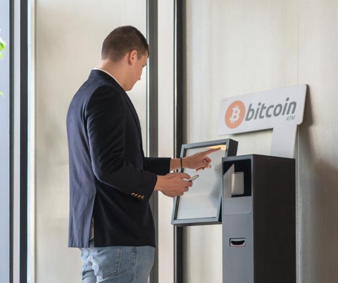 Young businessman buying cryptocurrency on ATM machine for buying and selling cryptocurrency.
