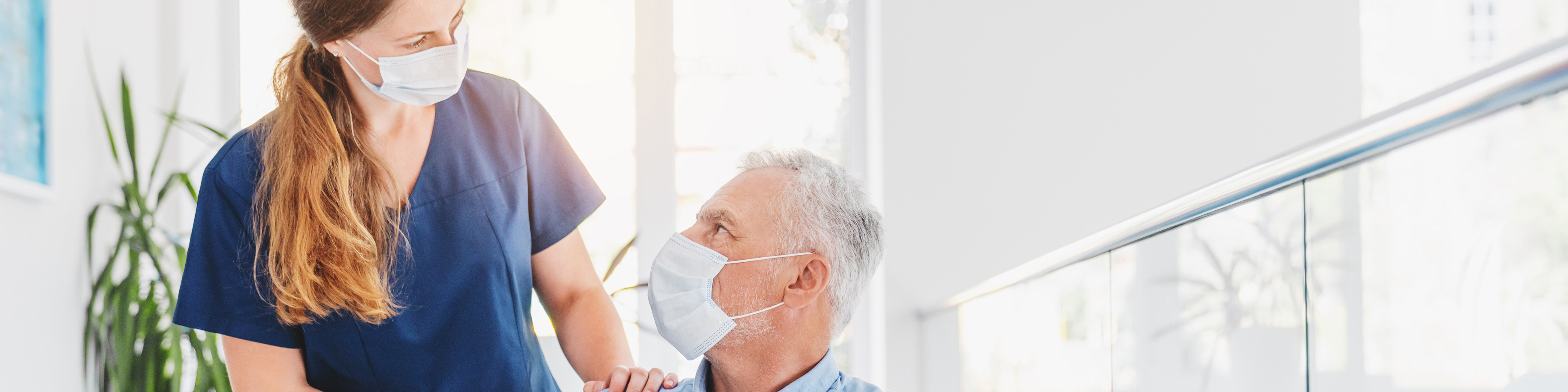 Nurse with face mask explaining information to face-masked male patient in wheelchair