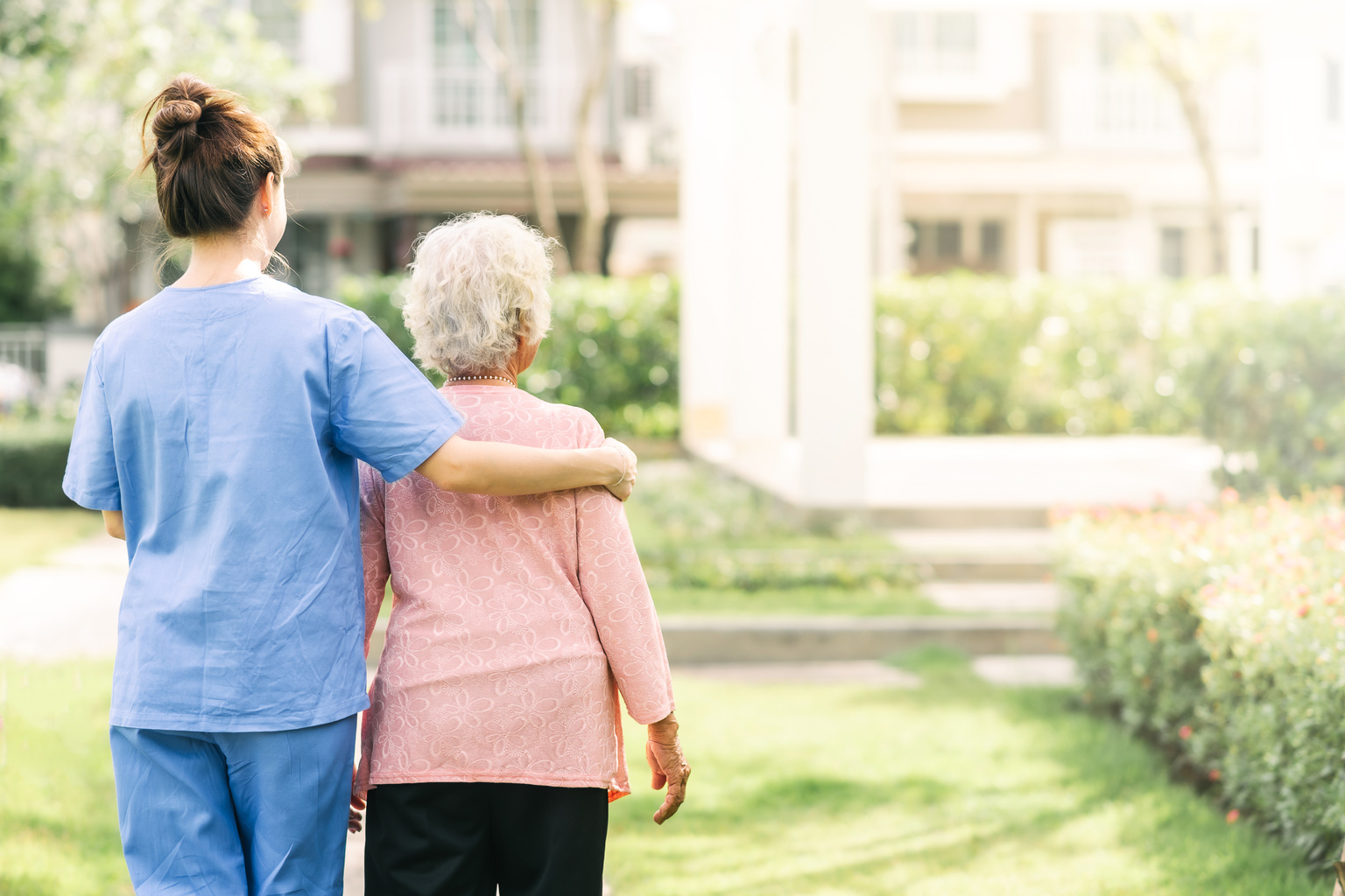 Certified nursing assistant helps senior patient walk around facility grounds