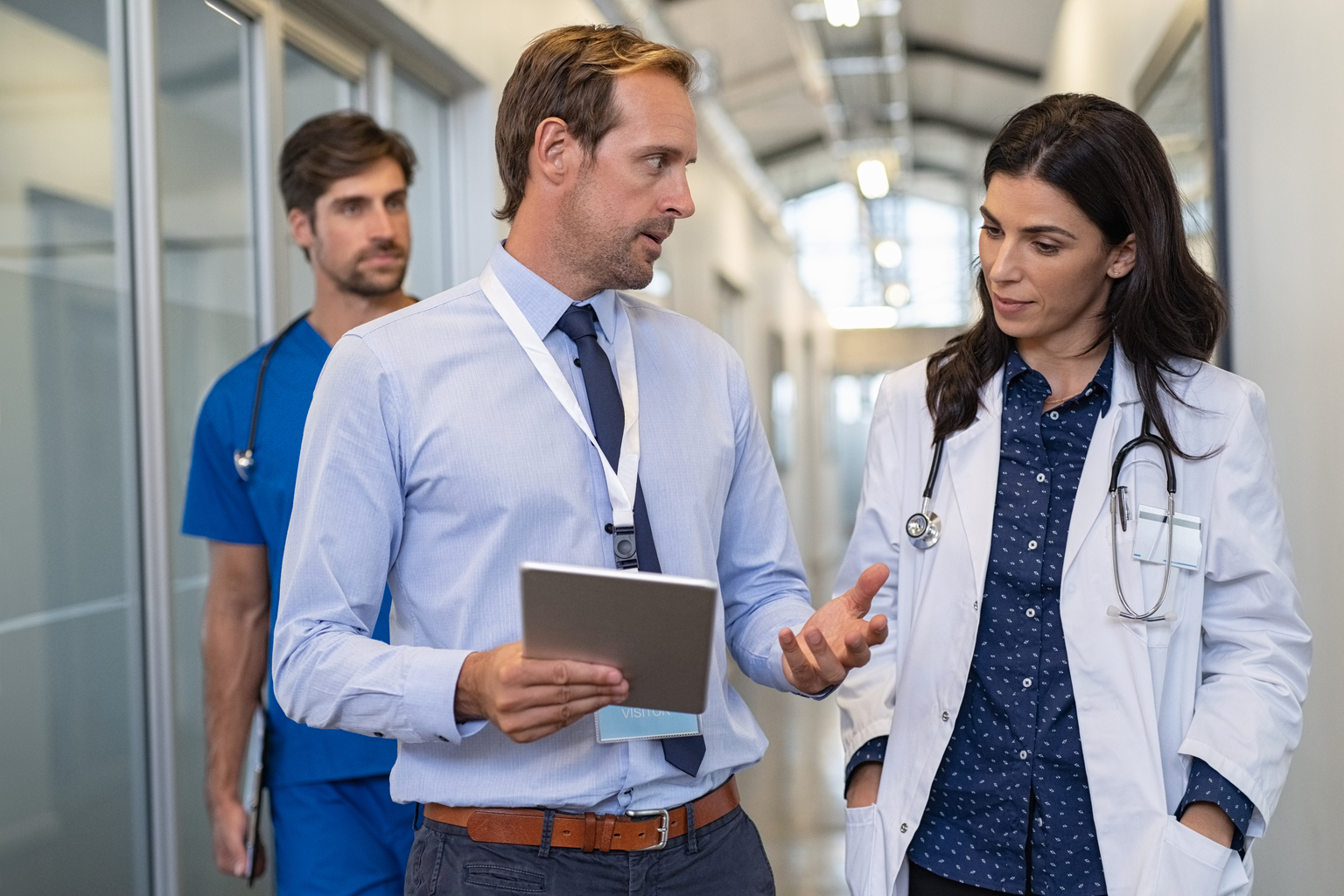 White male and female  doctor discussing in hospital hallway while holding digital tablet. 