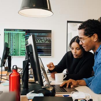 Focused male and female engineers coding over laptop on desk in office