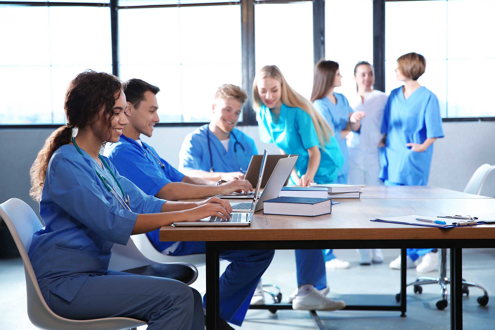 Group of nursing students conversing or working at laptops in a meeting room