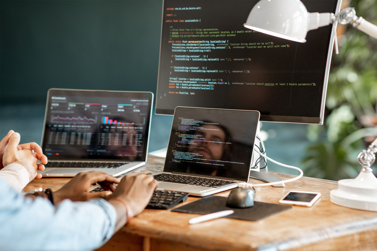 A man looking at computer code with two laptops and a large monitor.