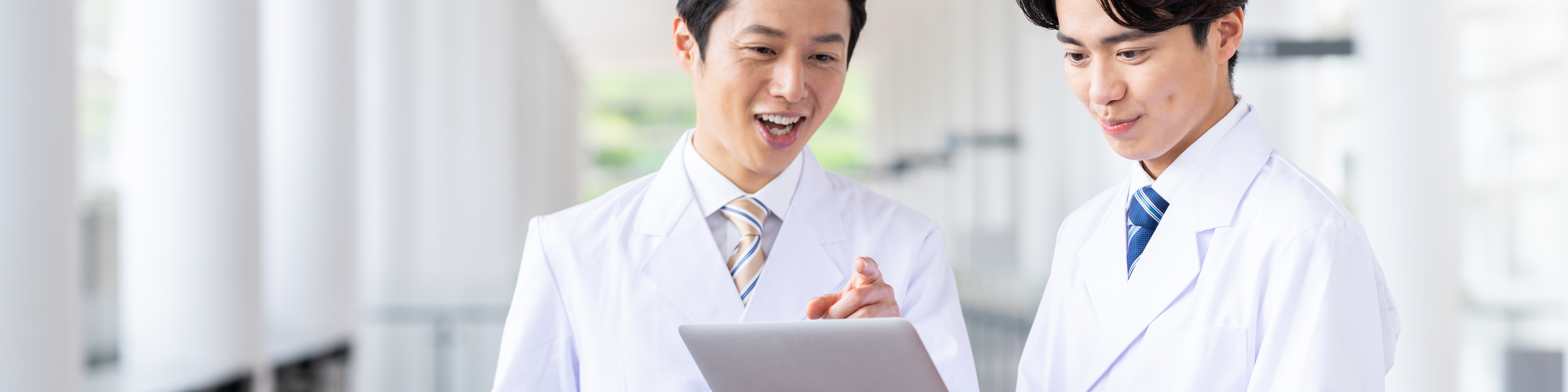 Two Japanese male doctors in white coats looking at laptop computer