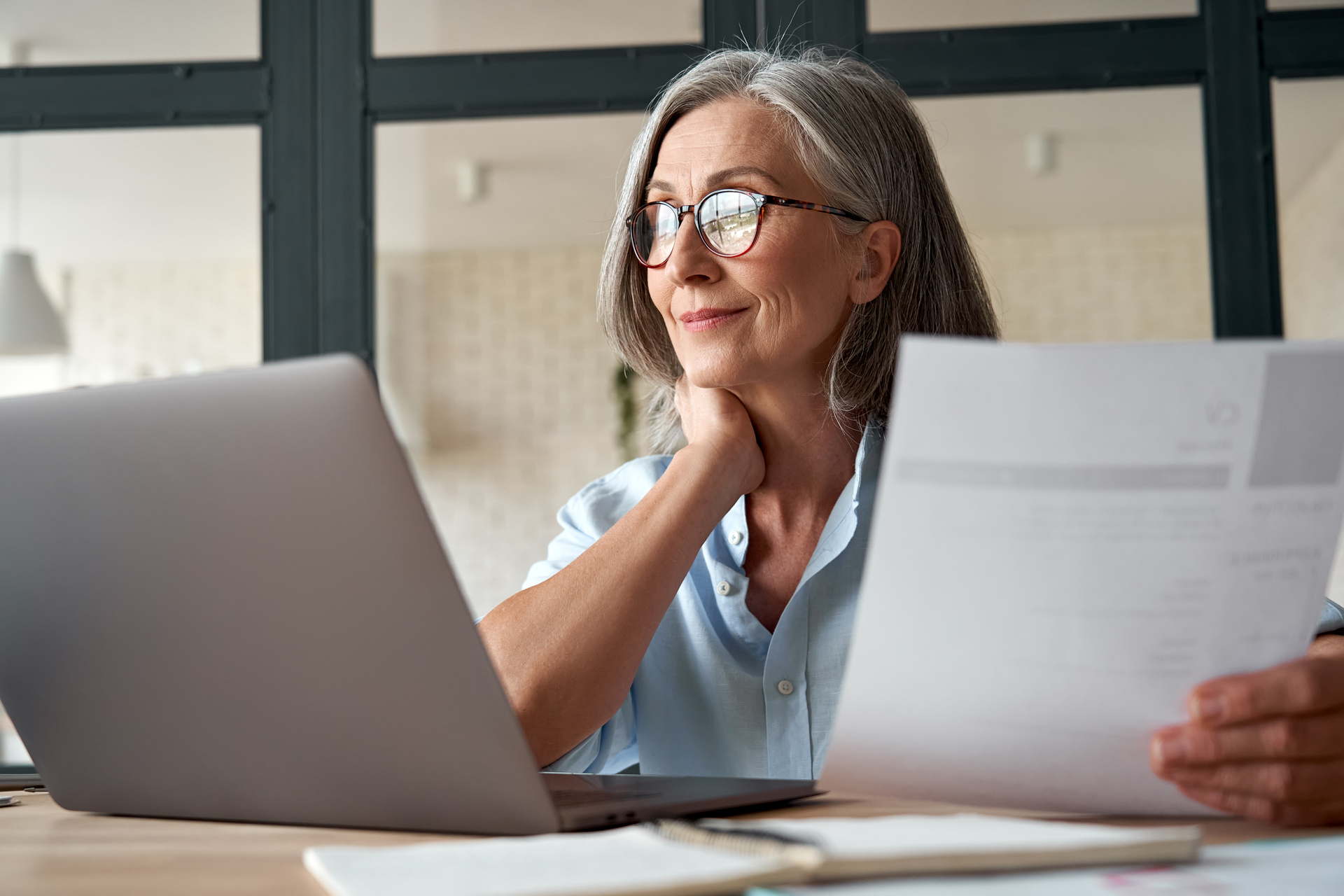 Smiling mature middle aged business woman using laptop working on computer sitting at desk.