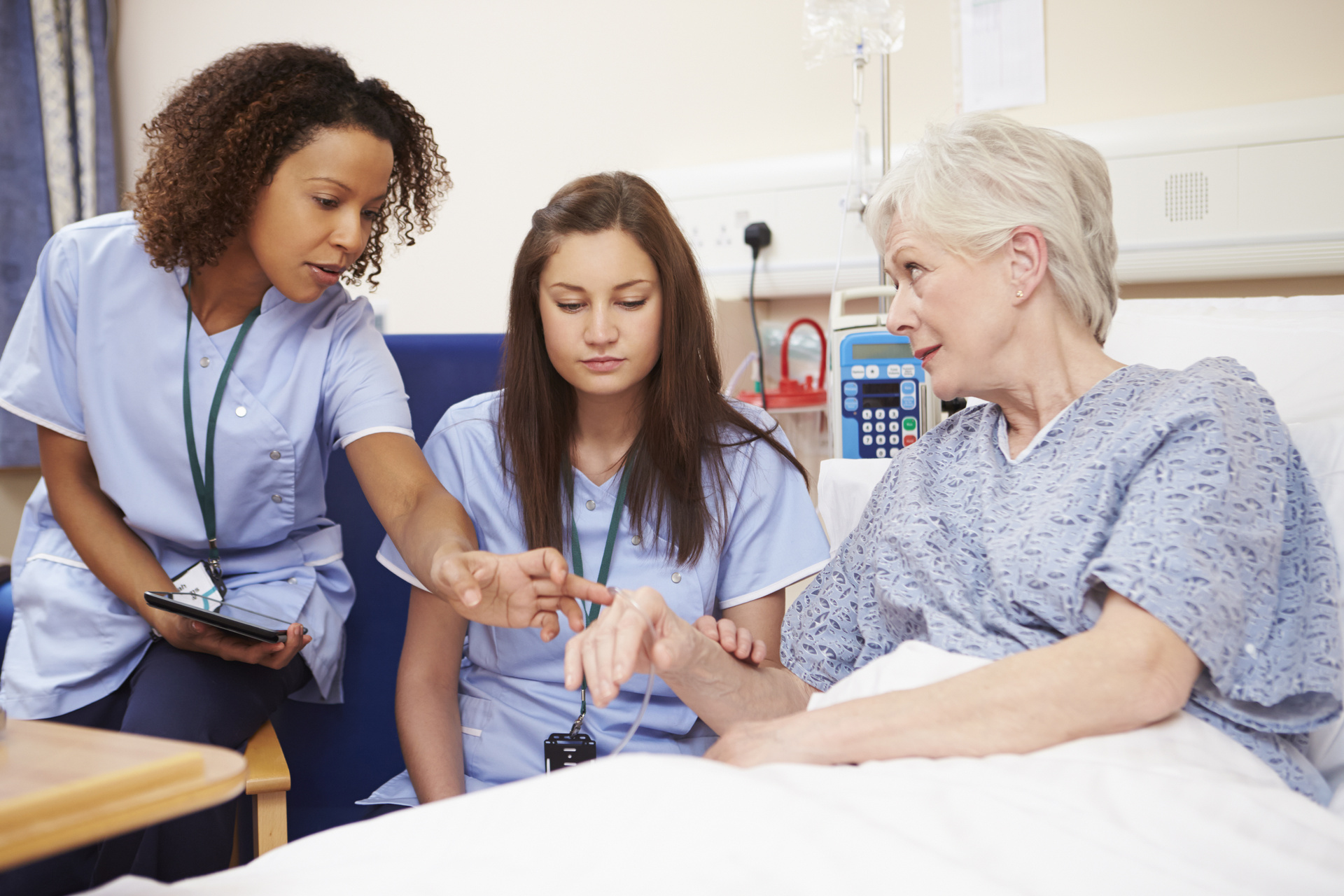 Trainee nurse sitting by female patient's bed in hospital