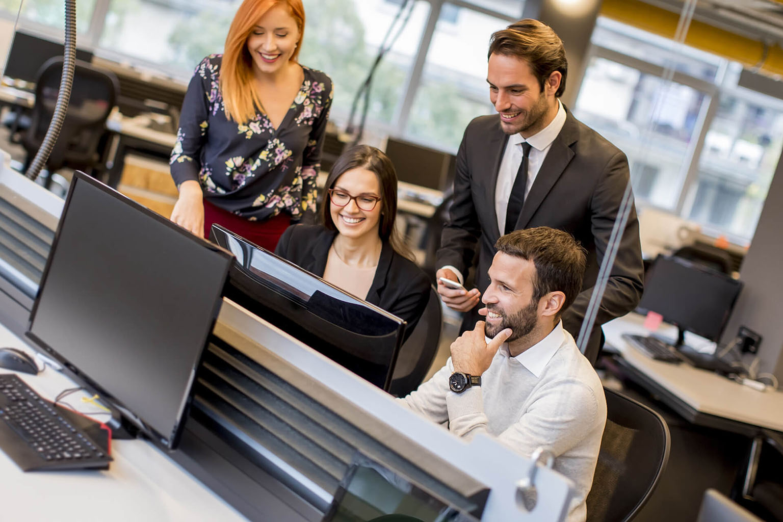 A group of happy employees gather around a computer to bill and invoice clients electronically.