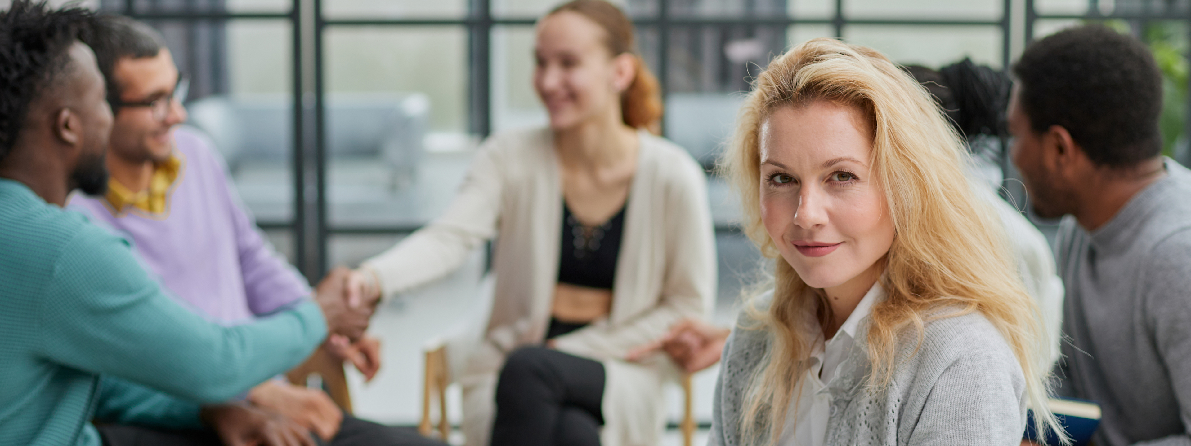 Smiling businesswoman looking at camera at seminar with her colleagues near by