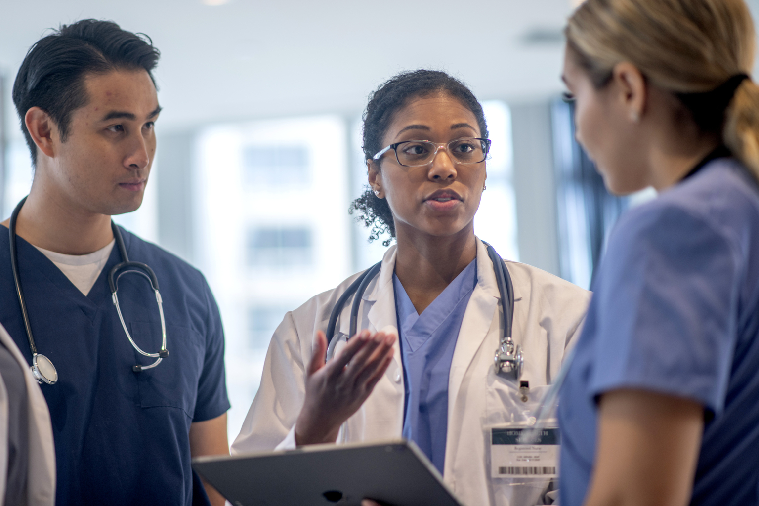 A small group of medial professionals stand together in the hallway while briefly meeting to go over a patient file