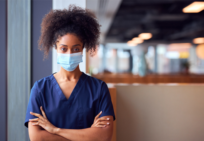 Nurse with folded arms, staring at camera, wearing face mask