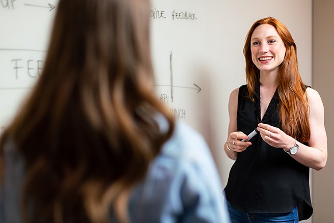 Two women brainstorming in meeting room with white board