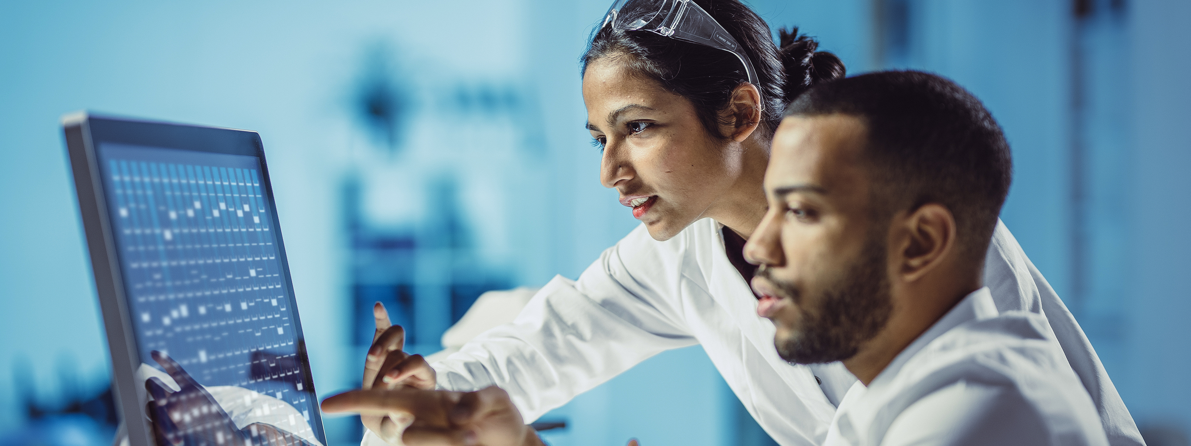 Two chemist in lab coat analyzing on a touch screen computer