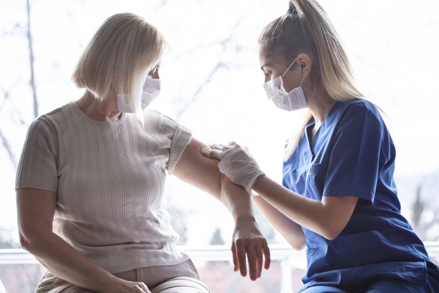 a young female nurse giving an older women a vaccine