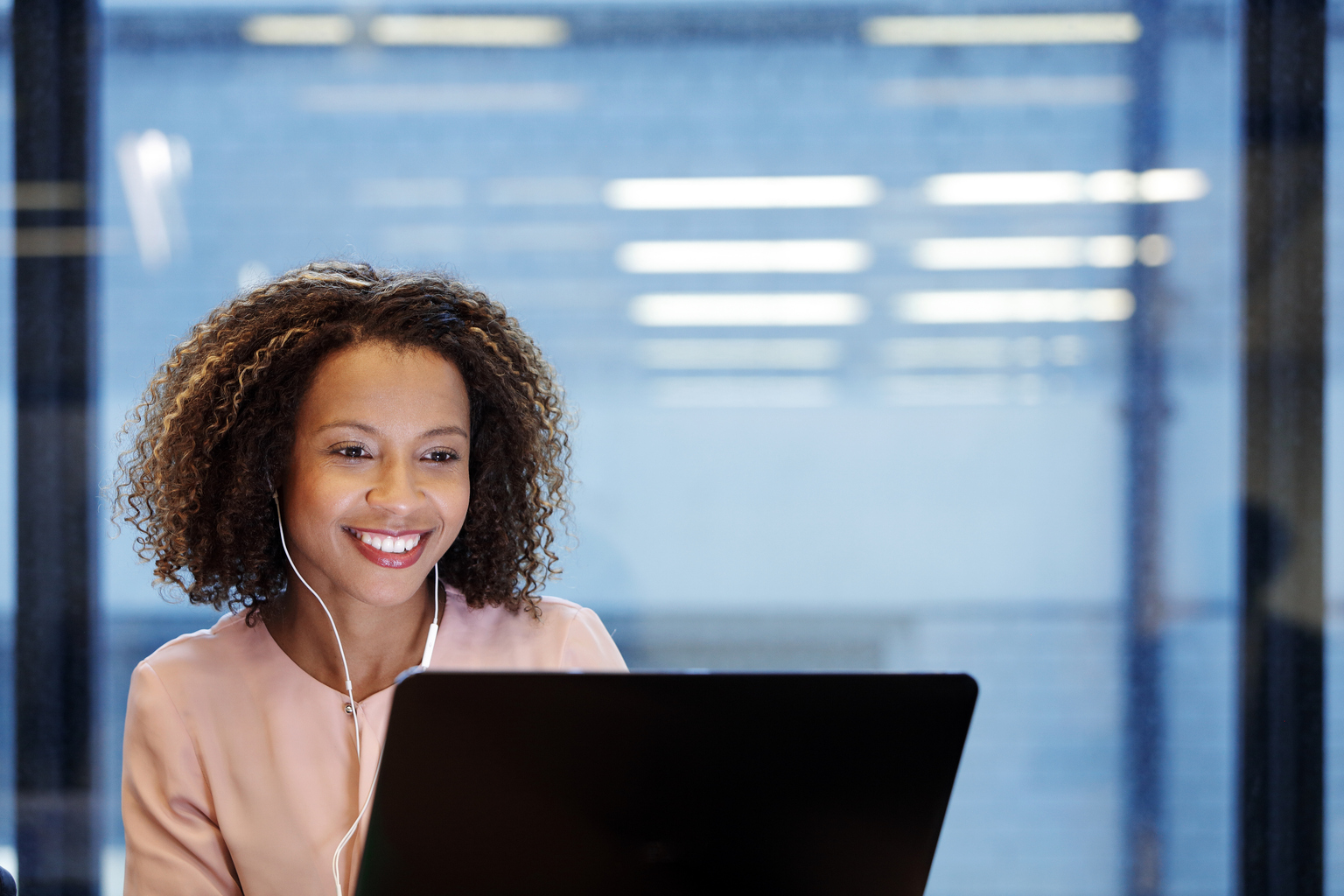 Young smiling businesswoman wearing earphones, using laptop