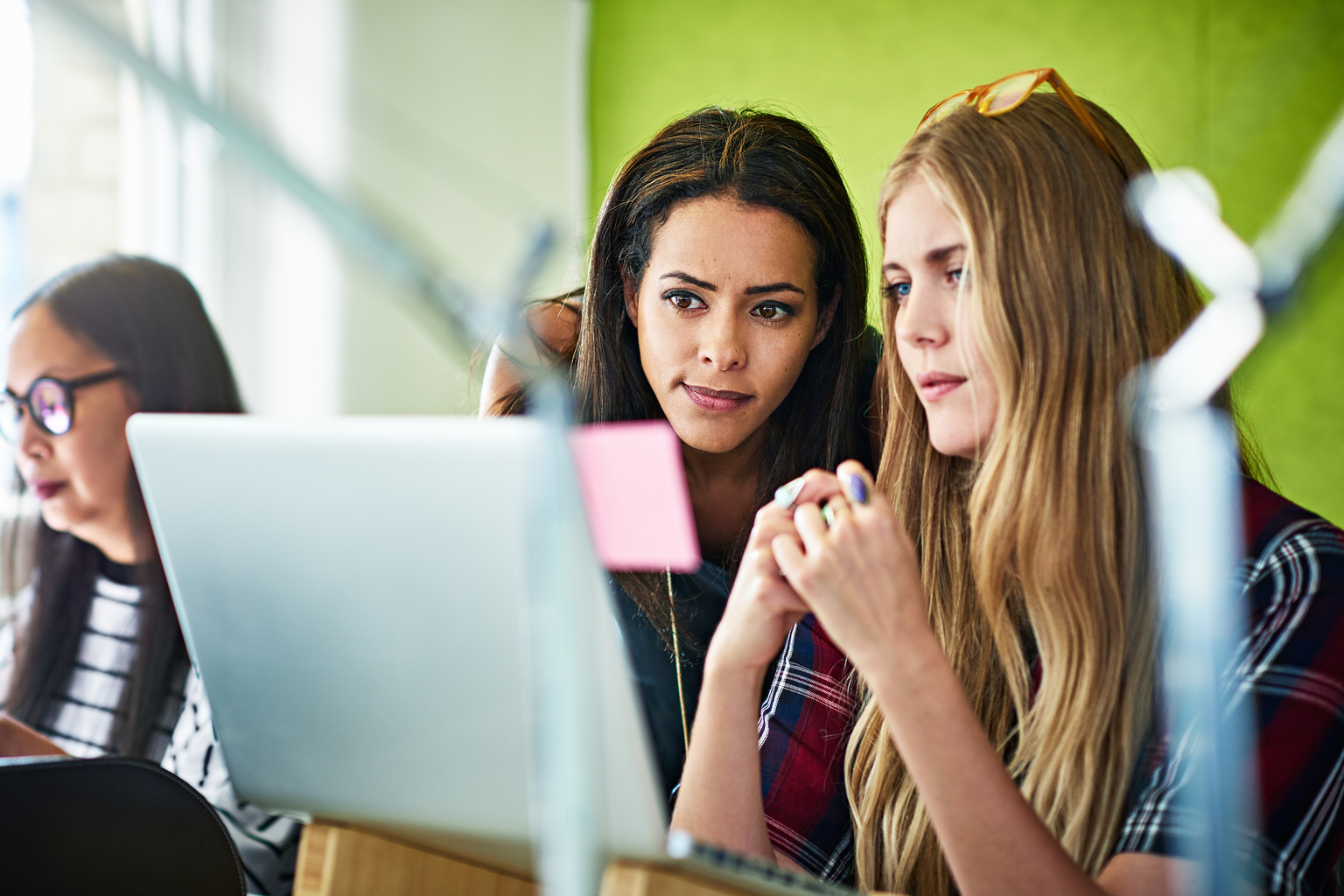 Two young businesswomen looking at laptop in office.