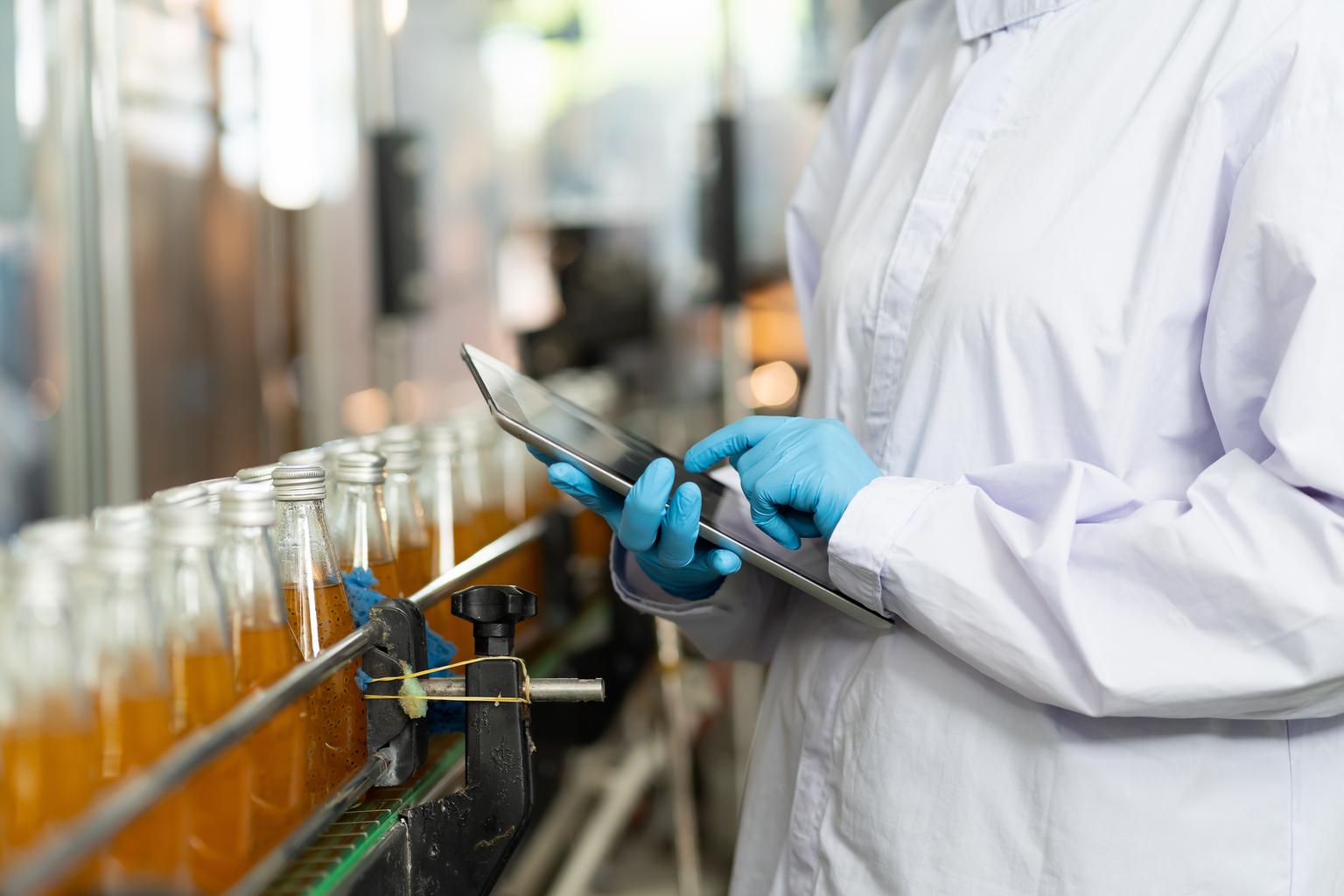 Hands of worker working with digital tablet check product on the conveyor belt in the beverage factory. Worker checking bottling line for processing. Inspection quality control