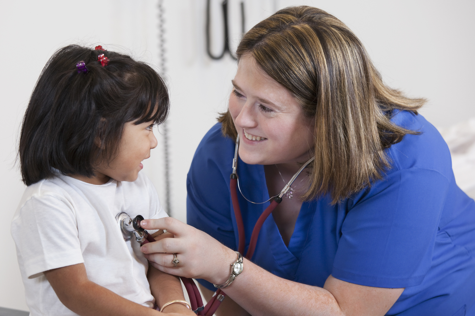 White female doctor checking girl patient's breathing in office.