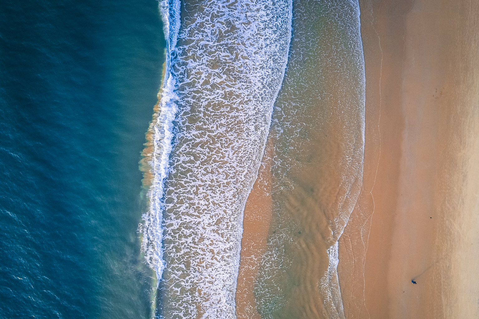 Aerial view of coastline with beach and ocean waves, taken by drone