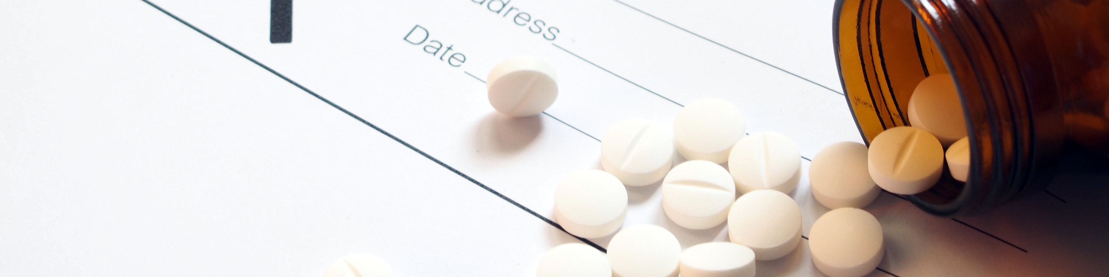 White tablets spilling out of brown glass bottle with blank Rx prescription form on wood table