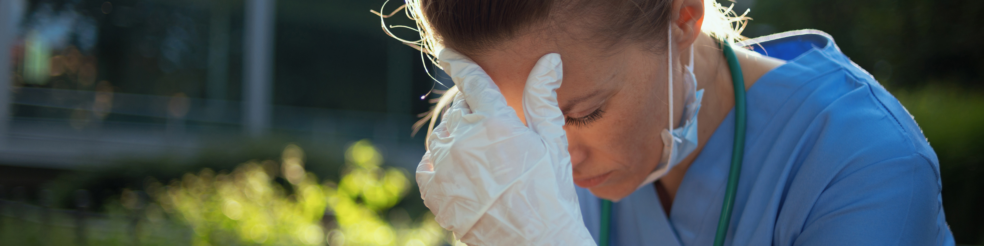 Medical practitioner woman sitting outdoors near hospital, propping head up with hand