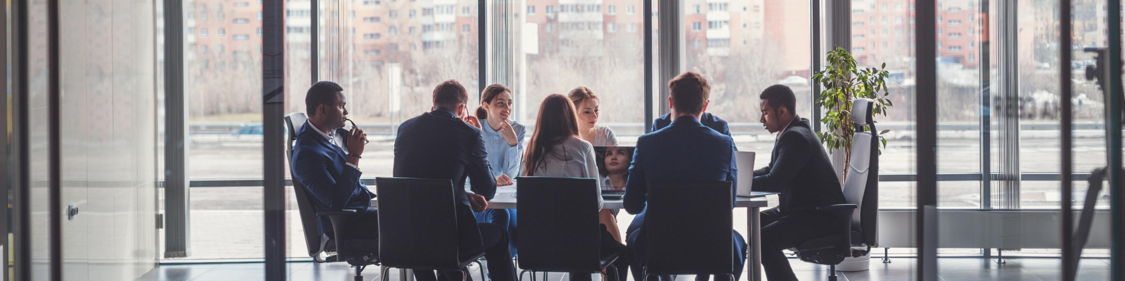 businesspeople sitting around a conference table in front of a wall of windows