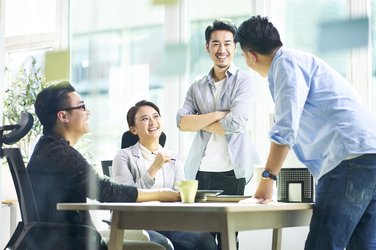Group of four happy young Asian corporate people teammates meeting discussing business in office