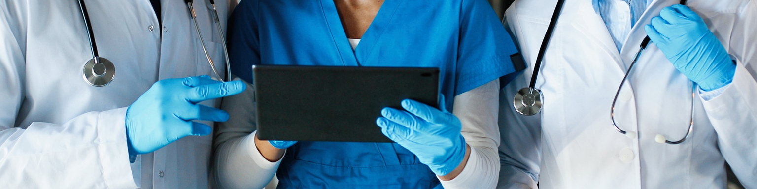 Mixed races male and females healthcare workers in hats medical masks and gloves walking in hospital and talking using tablet device