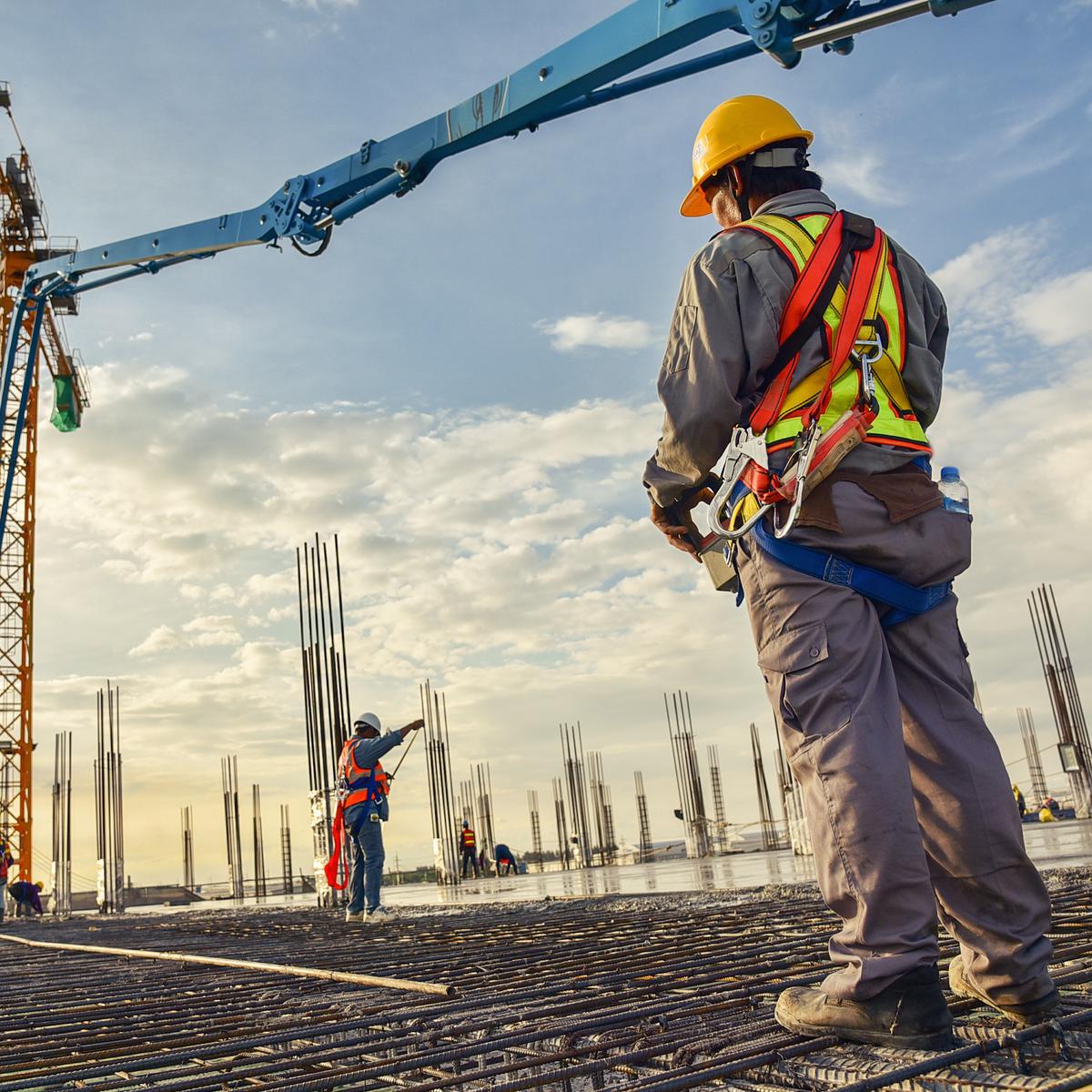 A construction worker control a pouring concrete pump on construction site and sunset background