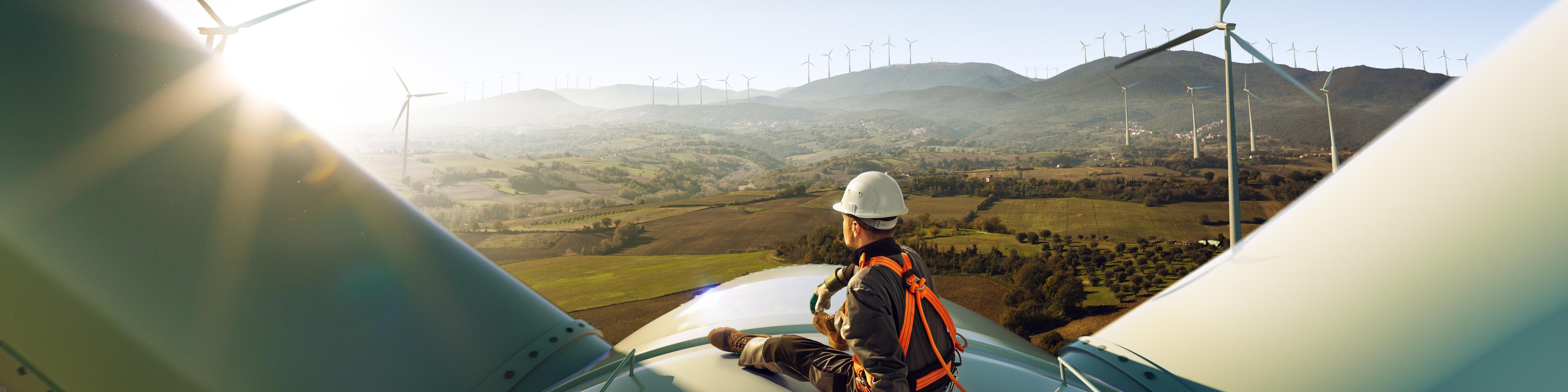 Happy engineer feel success after good work. He standing a top of windmill and looking beautiful sunset landscape